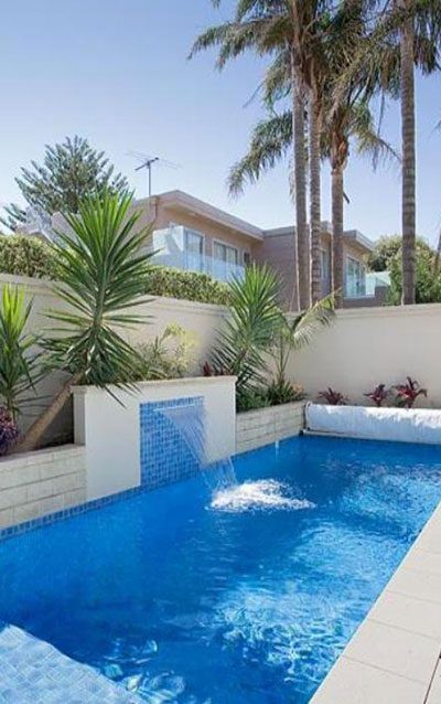 A pool with water flowing into it and palm trees in the background.