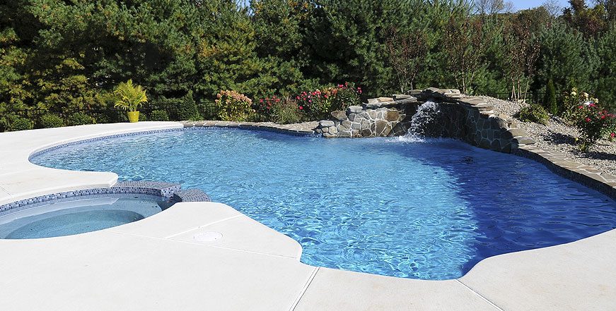 A pool with water falling into it and trees in the background.