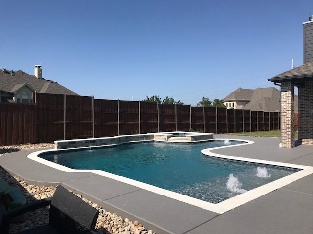 A pool with a stone surround and a concrete deck.